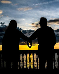 Silhouette man and woman standing by railing against sky during sunset