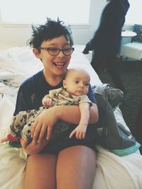 Happy boy carrying cute baby brother while sitting on bed at home