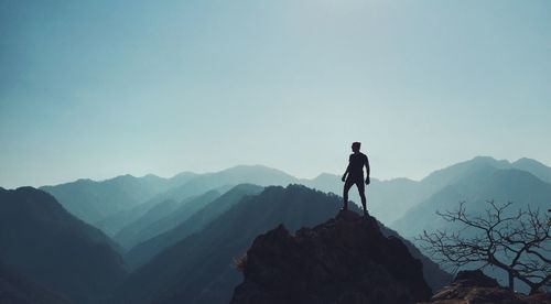 Silhouette man standing on cliff against clear sky during sunny day