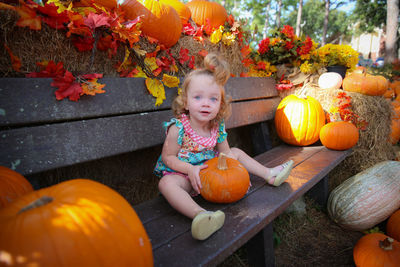 Portrait of girl sitting on bench amidst pumpkins at park during autumn