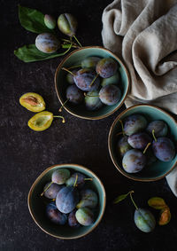 Overhead shot of bowls of fresh plums against a black background.