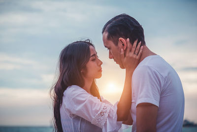 Side view of couple kissing against sky