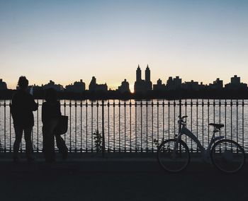 Silhouette people standing by river against clear sky