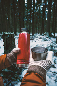 Cropped hands of woman having drink against trees in forest during winter