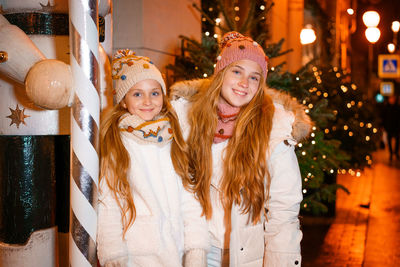 Lovely sisters teenagers walk on christmas eve along streets of evening city.