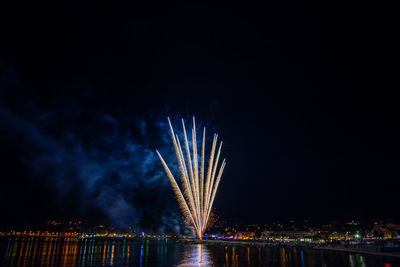 Firework display over illuminated cityscape against sky at night