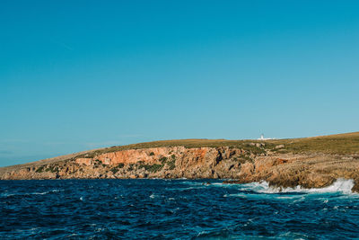 Scenic view of sea and cliff against clear blue sky