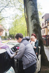 Father wearing shoes to daughter sitting on car