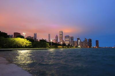 Illuminated buildings in city against sky during sunset