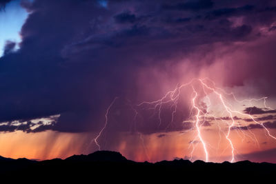 Low angle view of lightning over silhouette landscape at dusk