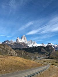 Road leading towards mountains against blue sky