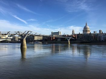 Bridge over river by buildings against sky