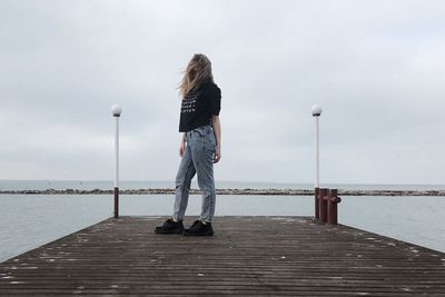 Rear view of woman standing on pier over sea against sky