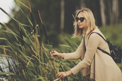 Side view of woman wearing sunglasses looking away while holding plant 