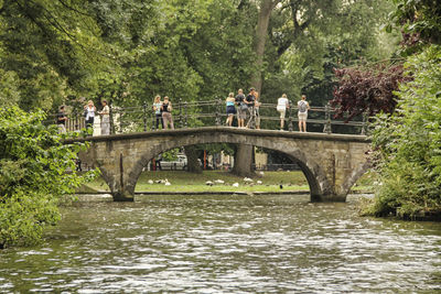 People on footbridge over river in forest