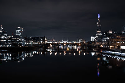 Illuminated buildings by river against sky at night