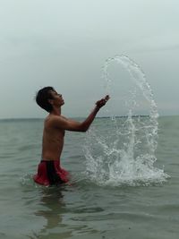 Shirtless man splashing water in sea against sky