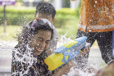 Side view of woman spraying water from gun while sitting outdoors