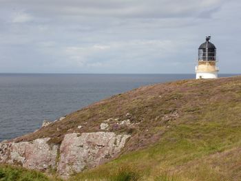 Lighthouse on cliff by sea against sky