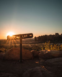 Sign board on land against sky during sunset