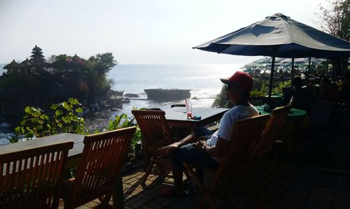 Woman sitting on chair at restaurant by sea against sky