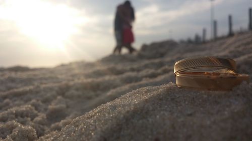 Close-up of wedding rings on sand with couple in background