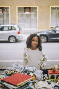 Portrait of smiling girl standing with hand on hip near stall at flea market