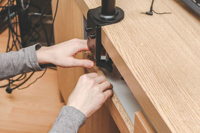 A young handsome caucasian guy sets a black bracket on the back side of a wooden desk .