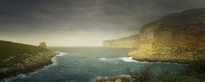 Scenic view of sea by cliff against sky