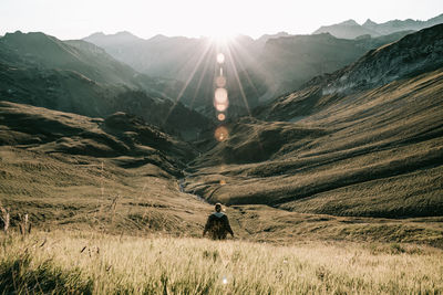 Rear view of man standing by grass against mountains