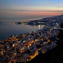 High angle view of illuminated city by sea against sky at sunset