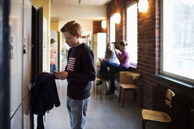 High school boy using mobile phone by locker