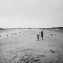 Rear view of woman and child with dog walking on beach against clear sky