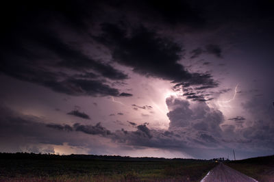 Road amidst field against lightning at night