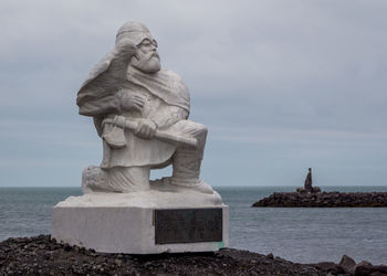 A rock sculpture of a viking and bird along the sea