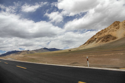 A flat, newly built wide asphalt road leads to the beautiful mountains in the distance