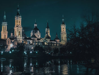 Illuminated buildings by river against sky at night