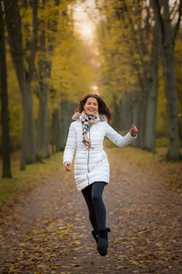 Full length of woman jumping while walking on road during autumn