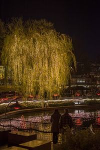 People standing by river against sky at night
