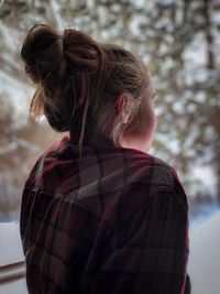 Rear view of woman looking through window while sitting at home