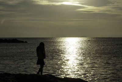 Silhouette people standing on sea against sky during sunset