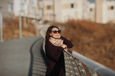 Portrait of woman standing by railing in city