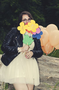Portrait of woman with balloons and toys standing against tree
