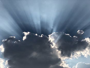 Low angle view of sunlight streaming through clouds