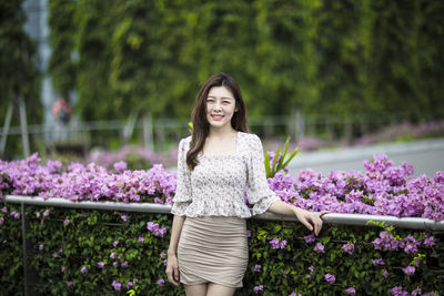 Portrait of smiling young woman standing by flowers at park