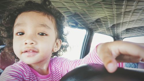 Close-up portrait of cute girl with curly hair sitting in car