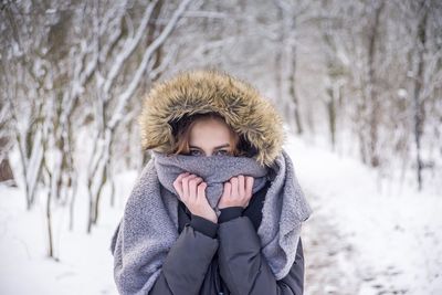 Portrait of girl standing snow covered land against trees