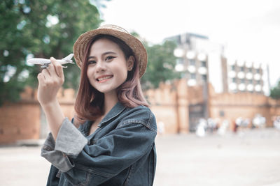 Portrait of smiling young woman standing against city in background