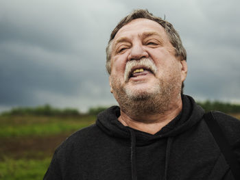 Close-up of serious senior man against cloudy sky