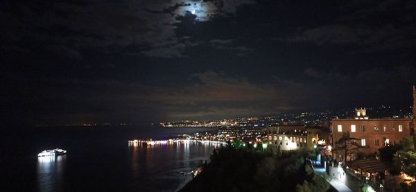 Illuminated city by sea against sky at night